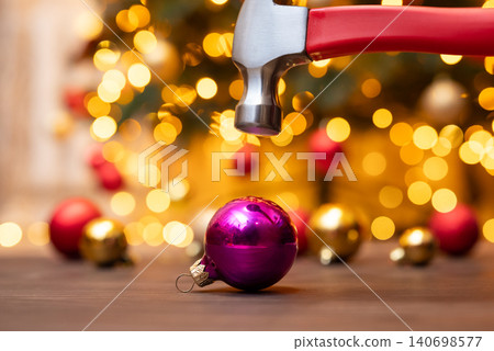 Hammer above the purple Christmas ball, festive decoration in the background, close up. Seconds before the bauble is broken, accident on winter holidays, no festive mood 140698577