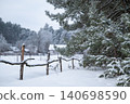 Rural landscape of winter in countryside. Old fence made of logs near pine trees with houses on the background 140698590