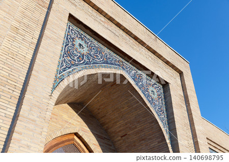Sunlit Islamic archway featuring intricate mosaic tilework set into a warm brick facade Sunlit Islamic archway featuring intricate mosaic tilework set into a warm brick facade 140698795