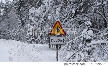 Triangular yellow warning sign with black snowflake symbol mounted on rusty post beside rural road, adjacent rectangular distance sign indicating 300 meters Triangular yellow warning sign with black snowflake symbol mounted on rusty post beside rural road, adjacent rectangular distance sign indicating 300 meters 140699515