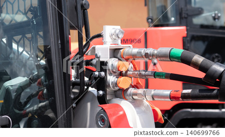 Close-up view of hydraulic hoses, metal couplings, and connectors mounted on heavy construction equipment with an orange machine body and industrial components in the background 140699766