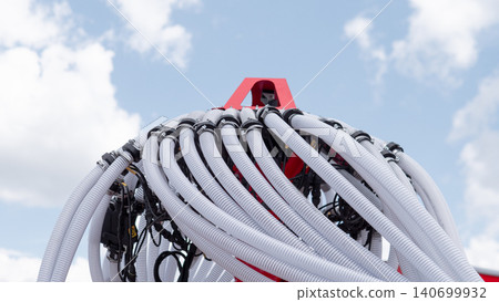 Close view of a large industrial machine with many thick flexible hoses and cables gathered around a red structural frame, set against a bright blue sky with scattered clouds 140699932