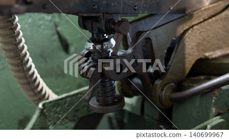 Tight view of metal linkage assembly connected to flexible corrugated hose mounted on aged green-painted industrial machine; visible threaded fittings, pivot Tight view of metal linkage assembly connected to flexible corrugated hose mounted on aged green-painted industrial machine; visible threaded fittings, pivot 140699967