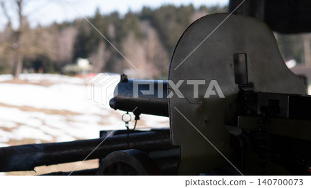 Close-up of antique field cannon barrel and partial shield positioned inside wooden shelter overlooking snow-covered meadow and distant tree line; soft Close-up of antique field cannon barrel and partial shield positioned inside wooden shelter overlooking snow-covered meadow and distant tree line; soft 140700073