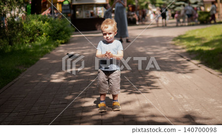Young boy in casual summer clothes walking along a tree-lined paved path in a public park Young boy in casual summer clothes walking along a tree-lined paved path in a public park 140700098