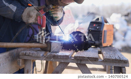 Portable Welder In Rugged Environment. Technician Manages Arc Sparks At Outdoor Site. Craftsman Skillfully Handles Welding Equipment Amidst Cold Outdoor Surroundings With Rugged Tools 140700524