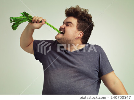 Diet, plus size and man eating vegetable for health benefit, nutrition and wellness in studio in white background. Weight loss, celery stick and male person for healthy food, wellbeing and detox 140700547