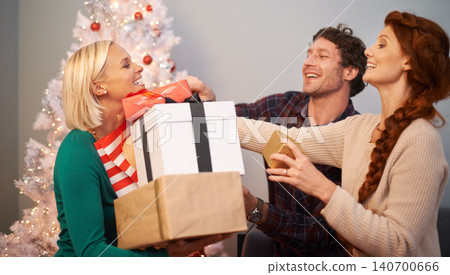 Friends, Christmas and present for celebration at tree for festive season or giving gift box, vacation or holiday. Man, women and parcel in living room for winter break or excited, bonding or love Friends, Christmas and present for celebration at tree for festive season or giving gift box, vacation or holiday. Man, women and parcel in living room for winter break or excited, bonding or love 140700666