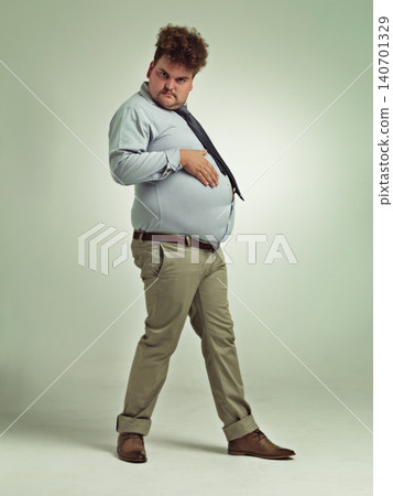Business man, portrait and plus size with stomach gesture and silly in a studio with funny joke. Goofy, employee and office fashion with fun and work clothing with green background and humor Business man, portrait and plus size with stomach gesture and silly in a studio with funny joke. Goofy, employee and office fashion with fun and work clothing with green background and humor 140701329