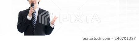 一位年輕的商人手持麥克風進行演講;一位公司員工在培訓課程或講座上發言;一條沒有面孔的橫幅。 一位年輕的商人手持麥克風進行演講;一位公司員工在培訓課程或講座上發言;一條沒有面孔的橫幅。 140701357