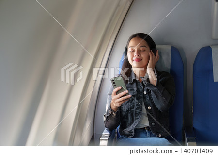 Asian woman listening to music with headphones on airplane flight Asian woman listening to music with headphones on airplane flight 140701409