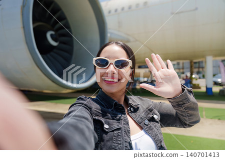 Happy Asian woman tourist taking selfie and waving near airplane for summer travel vacation Happy Asian woman tourist taking selfie and waving near airplane for summer travel vacation 140701413