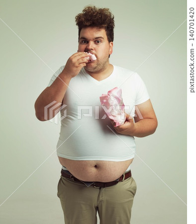 Plus size, candy and portrait for man in studio with marshmallow for unhealthy eating, sugar and confection. Young person with sweets in mouth and round stomach for greed, comedy and humor indoor Plus size, candy and portrait for man in studio with marshmallow for unhealthy eating, sugar and confection. Young person with sweets in mouth and round stomach for greed, comedy and humor indoor 140701420