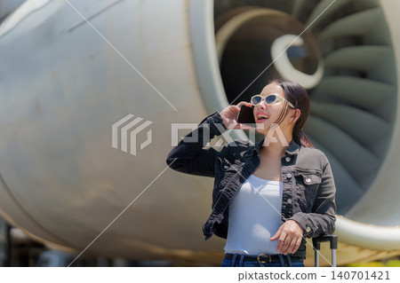 Asian woman talking on smartphone near airplane jet engine at airport Asian woman talking on smartphone near airplane jet engine at airport 140701421
