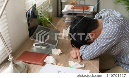 Exhausted Asian man sleeping on desk with laptop and crumpled tissues for burnout concept 140701517