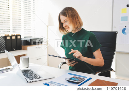 Concept of business working, Businesswoman sitting while writing and checking business analytic document report and holding tablet with computer pc, smartphone on desk in her workstation. Concept of business working, Businesswoman sitting while writing and checking business analytic document report and holding tablet with computer pc, smartphone on desk in her workstation. 140701628