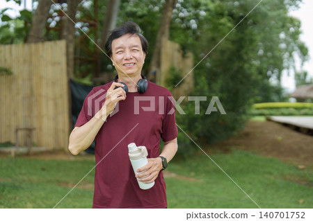 Smiling senior Asian man holding water bottle in park for healthy lifestyle Smiling senior Asian man holding water bottle in park for healthy lifestyle 140701752
