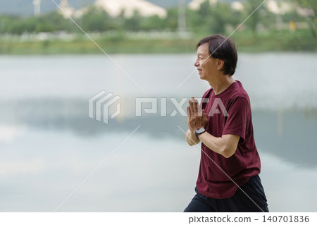 Mature Asian man meditating with hands in prayer position by lake Mature Asian man meditating with hands in prayer position by lake 140701836