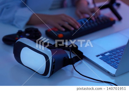 Hands typing on keyboard with virtual reality VR headset and laptop for immersive gaming technology 140701951