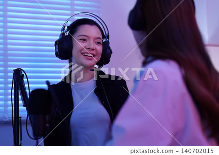 Smiling young Asian woman wearing headset with microphone podcasting or streaming gaming content creation indoors Smiling young Asian woman wearing headset with microphone podcasting or streaming gaming content creation indoors 140702015