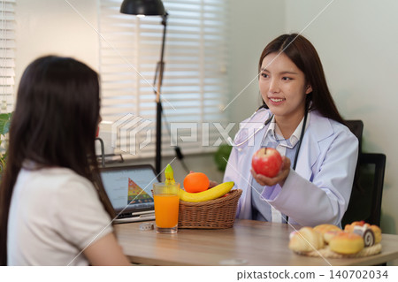 Asian nutritionist doctor giving healthy eating diet wellness consultation to patient in office holding apple Asian nutritionist doctor giving healthy eating diet wellness consultation to patient in office holding apple 140702034