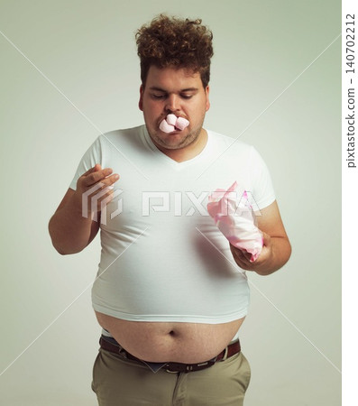 Obesity, weight gain and humor for man in studio with marshmallow for unhealthy eating, sugar and candy. Overweight person with sweets in mouth and fat stomach for greed, comedy and funny indoor Obesity, weight gain and humor for man in studio with marshmallow for unhealthy eating, sugar and candy. Overweight person with sweets in mouth and fat stomach for greed, comedy and funny indoor 140702212