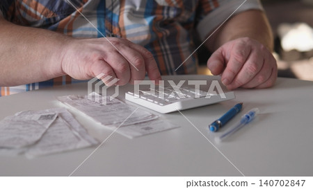 A man is focused on a calculator while organizing receipts and pens on a table. The scene shows attention to detail as he manages his financial records. A man is focused on a calculator while organizing receipts and pens on a table. The scene shows attention to detail as he manages his financial records. 140702847
