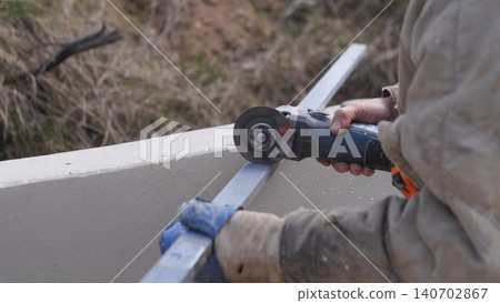 Maintenance Worker Grinding Outdoor Metal Rail On Concrete Barrier, Gloved Hands Steadying Grinder, Daylight Repair Scene With Sparks And Dust, Practical Upkeep And Site Durability Focus 140702867
