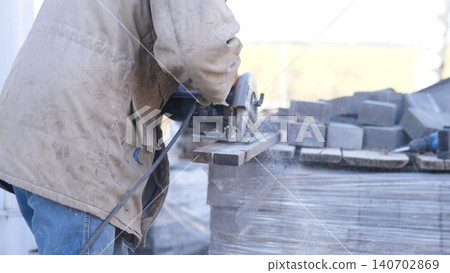 Worker Cutting Concrete Blocks With Grinder, Sparks And Dust Flying, Closeup Of Abrasive Wheel Shaping Block Edges On Wet Workbench, Protective Gloves And Heavy Motor Visible, Industrial Worker Cutting Concrete Blocks With Grinder, Sparks And Dust Flying, Closeup Of Abrasive Wheel Shaping Block Edges On Wet Workbench, Protective Gloves And Heavy Motor Visible, Industrial 140702869