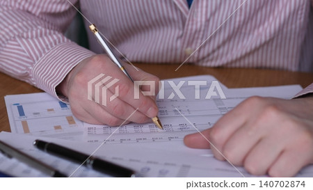 Hands Annotating Financial Report With Pencil, Closeup Of Charts And Figures On Desk, Documents Arranged With Calculator And Pens, Analytical Atmosphere Conveying Budgeting, Audit Or Tax Hands Annotating Financial Report With Pencil, Closeup Of Charts And Figures On Desk, Documents Arranged With Calculator And Pens, Analytical Atmosphere Conveying Budgeting, Audit Or Tax 140702874