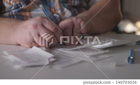 A person writes notes on various receipts and uses a calculator. The scene shows a cluttered table with papers and tools needed for managing expenses. A person writes notes on various receipts and uses a calculator. The scene shows a cluttered table with papers and tools needed for managing expenses. 140703016