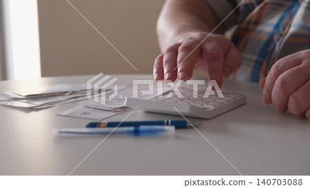 A person is counting bills and managing expenses on a calculator at a table. Receipts are spread out around them as they focus on their finances. A person is counting bills and managing expenses on a calculator at a table. Receipts are spread out around them as they focus on their finances. 140703088