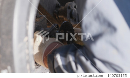 Mechanic Working On Undercarriage Components Near Wheel Hub, Hands Tightening Bolts And Checking Suspension Mounts, Dirty Gloves, Workshop Light And Practical Repair Focus 140703155