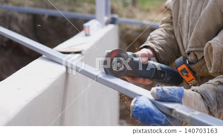 Site Worker Finishing Metal Rail With Grinder Wheel, Gloved Hands Smoothing Surface Near Concrete Edge, Sparks And Rotating Disc Visible, Quality Control And Alignment For Installation Site Worker Finishing Metal Rail With Grinder Wheel, Gloved Hands Smoothing Surface Near Concrete Edge, Sparks And Rotating Disc Visible, Quality Control And Alignment For Installation 140703163