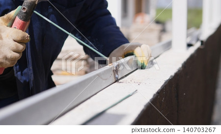 Closeup Metalworker Welding Joint, Sparks And Molten Bead Visible, Gloved Hand Steadying Bracket On Metal Profile, Industrial Site Background, Precise Joiner Action And Heat Intensity 140703267