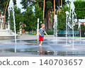 Child playing with water fountain in city square on summer day. Summer lifestyle, joy, freedom and refreshing activity in urban environment. 140703657