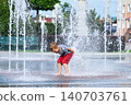 Child playing with water fountain in city square on summer day. Summer lifestyle, joy, freedom and refreshing activity in urban environment. 140703761