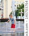 Child playing with water fountain in city square on summer day. Summer lifestyle, joy, freedom and refreshing activity in urban environment. 140703764