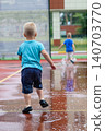 Children riding balance bikes through puddles on wet outdoor sports court after rain. Outdoor lifestyle, childhood activity, freedom and play in urban environment. 140703770