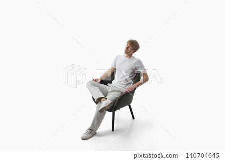 Relaxed teen boy sitting on chair in white studio space. Relaxed teen boy sitting on chair in white studio space. 140704645