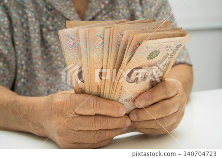 Asian elder senior woman patient holding Thai banknotes money in her hand, Cost of living and medical care. Asian elder senior woman patient holding Thai banknotes money in her hand, Cost of living and medical care. 140704723