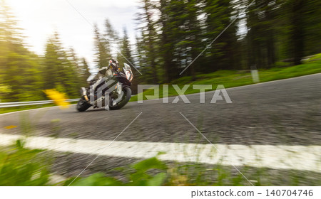 Sport motorcycle rider cornering on a winding mountain pass. Motion blur and dynamic perspective emphasize speed, control, performance riding and scenic road adventure. Sport motorcycle rider cornering on a winding mountain pass. Motion blur and dynamic perspective emphasize speed, control, performance riding and scenic road adventure. 140704746