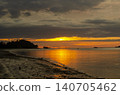 Golden sunset reflecting across still coastal waters with dramatic clouds enhancing the scenic shoreline view 140705462