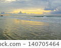 Coastal sunset panorama with warm golden light reflecting on shallow shoreline waters beneath layered clouds 140705464