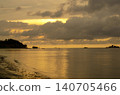 Low-tide beach scene illuminated by a golden sunset casting warm reflections over wet sand and calm waters 140705466