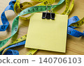 Measuring tape wrapped around a blank sticky note symbolizing diet planning with customizable space for text 140706103