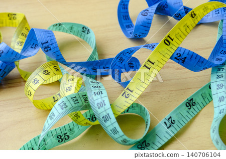 Multiple measuring tapes scattered across a wooden surface representing fitness planning and lifestyle improvement efforts 140706104