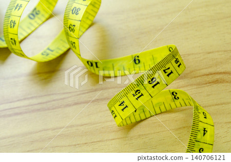 Yellow measuring tape arranged on a wooden surface representing fitness progress measurement Yellow measuring tape arranged on a wooden surface representing fitness progress measurement 140706121