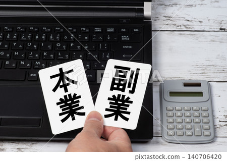 A business image of someone sitting in front of a computer, holding cards labeled "main job" and "side job." A business image of someone sitting in front of a computer, holding cards labeled "main job" and "side job." 140706420