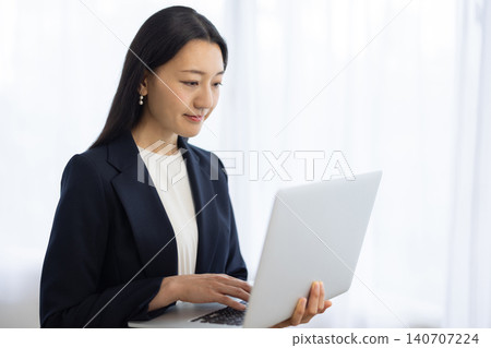 A young Japanese businesswoman is using her laptop by the window. A young Japanese businesswoman is using her laptop by the window. 140707224